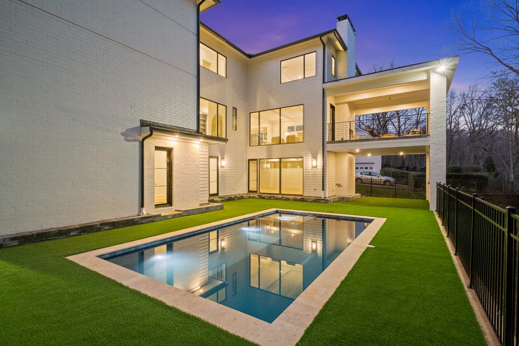 Lap pool and lit terrace at dusk behind a modern white brick house