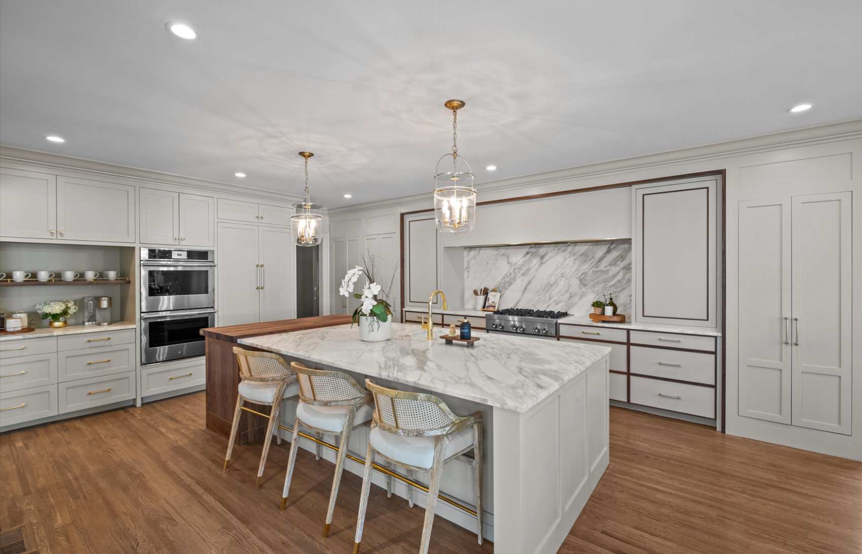 Kitchen with a marble island, panelled cabinetry and brass pendant lights